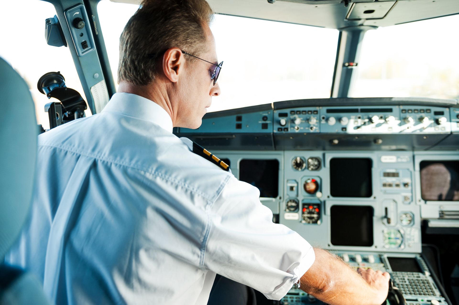 Pilot in white shirt operating controls in an airplane cockpit.