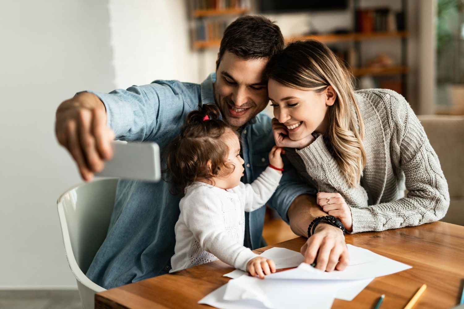 Family taking a selfie at a table while a toddler reaches toward the phone