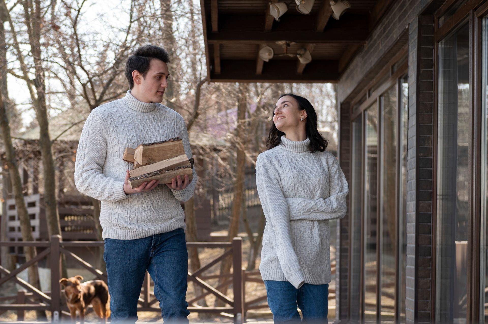 Two people standing on a wooden porch, talking, with a dog in the background.