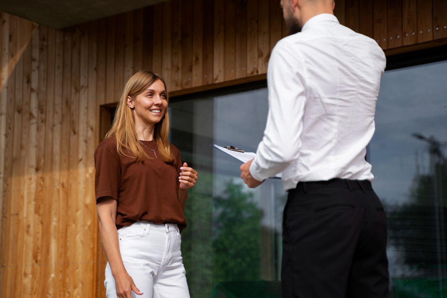 Two people talking outside a wooden building, one holding a key and smiling.