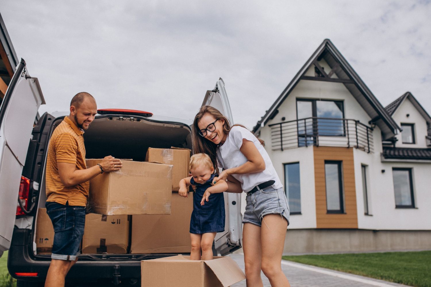People unpacking boxes from a van outside a suburban house