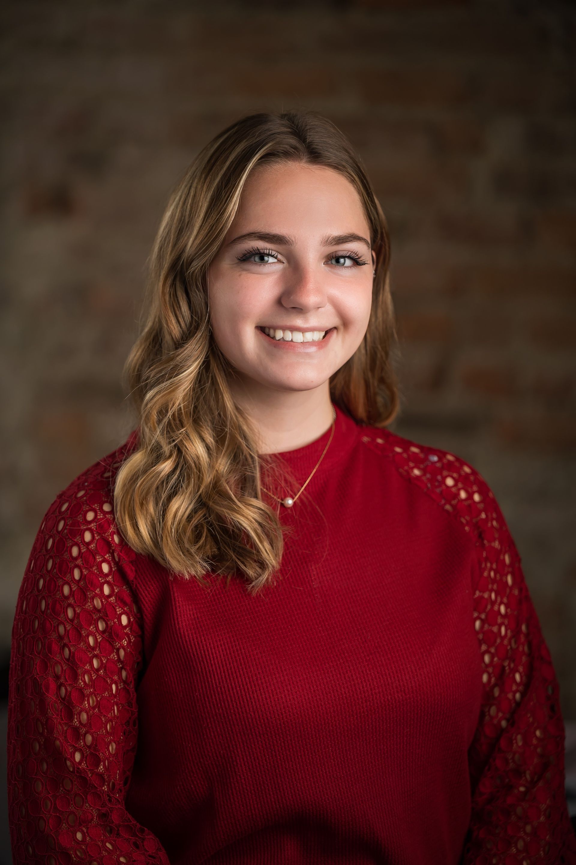 Smiling person in a red sweater against a blurred brown background