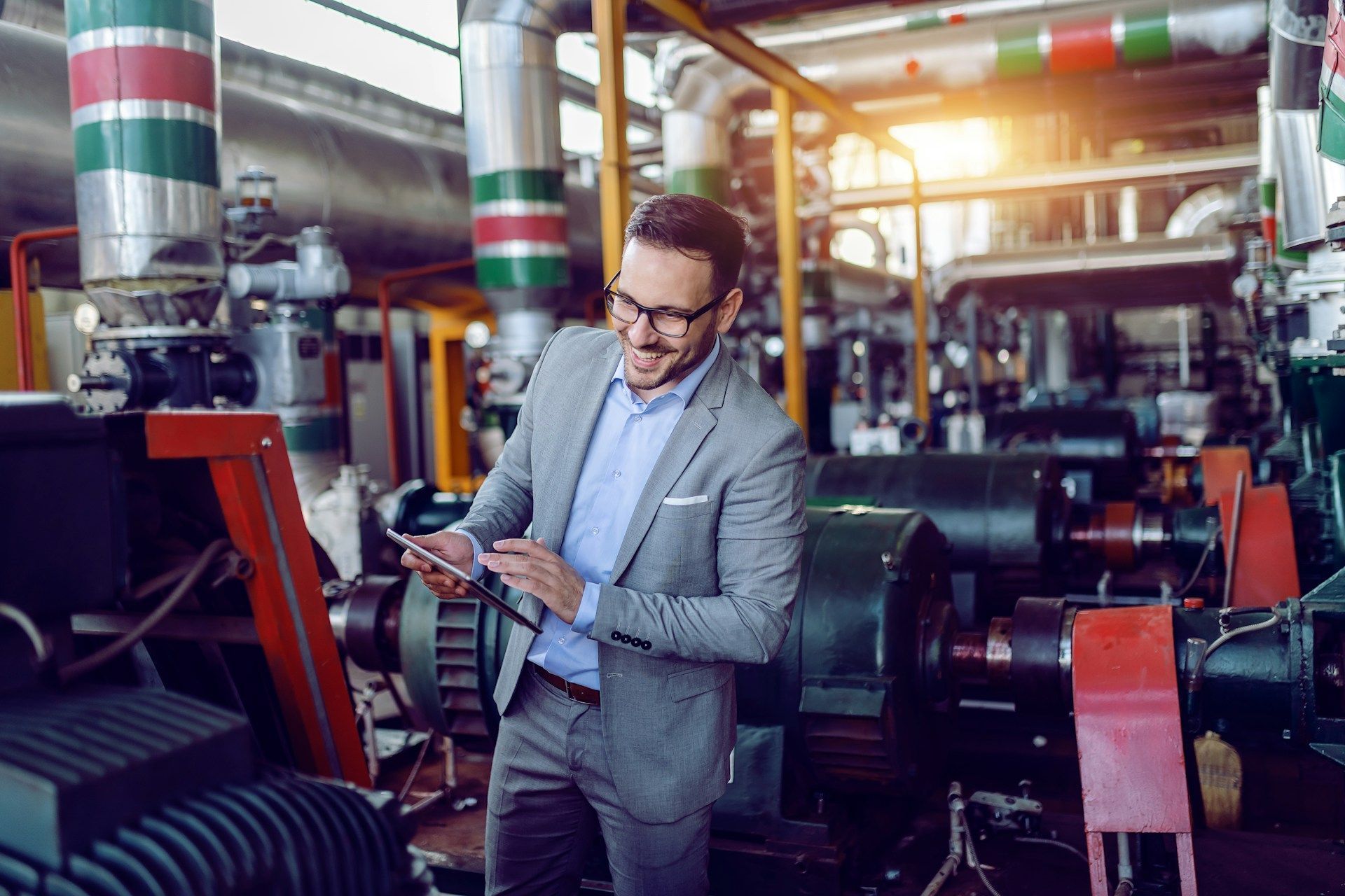 Man in a gray blazer using a tablet in an industrial factory with colorful columns and machinery