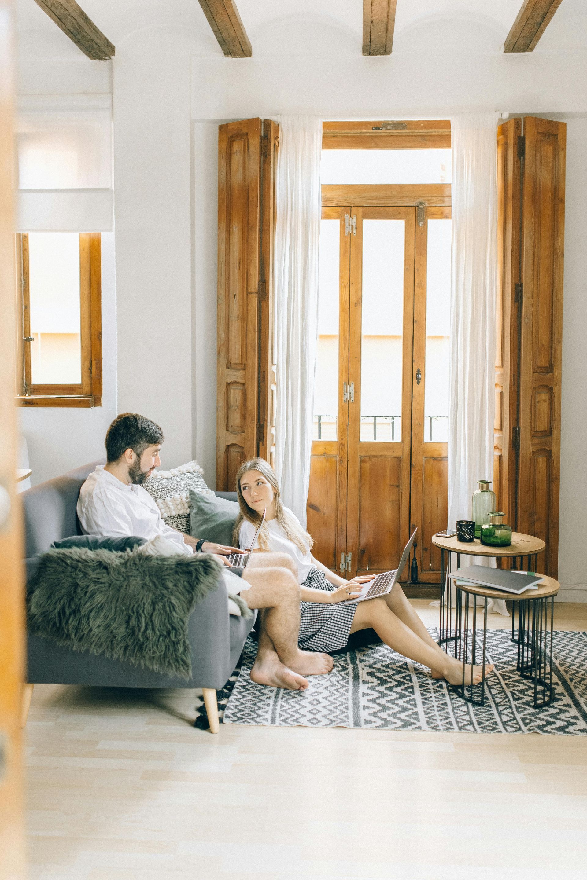 Living room with two people on a sofa near a bright window and wooden doors