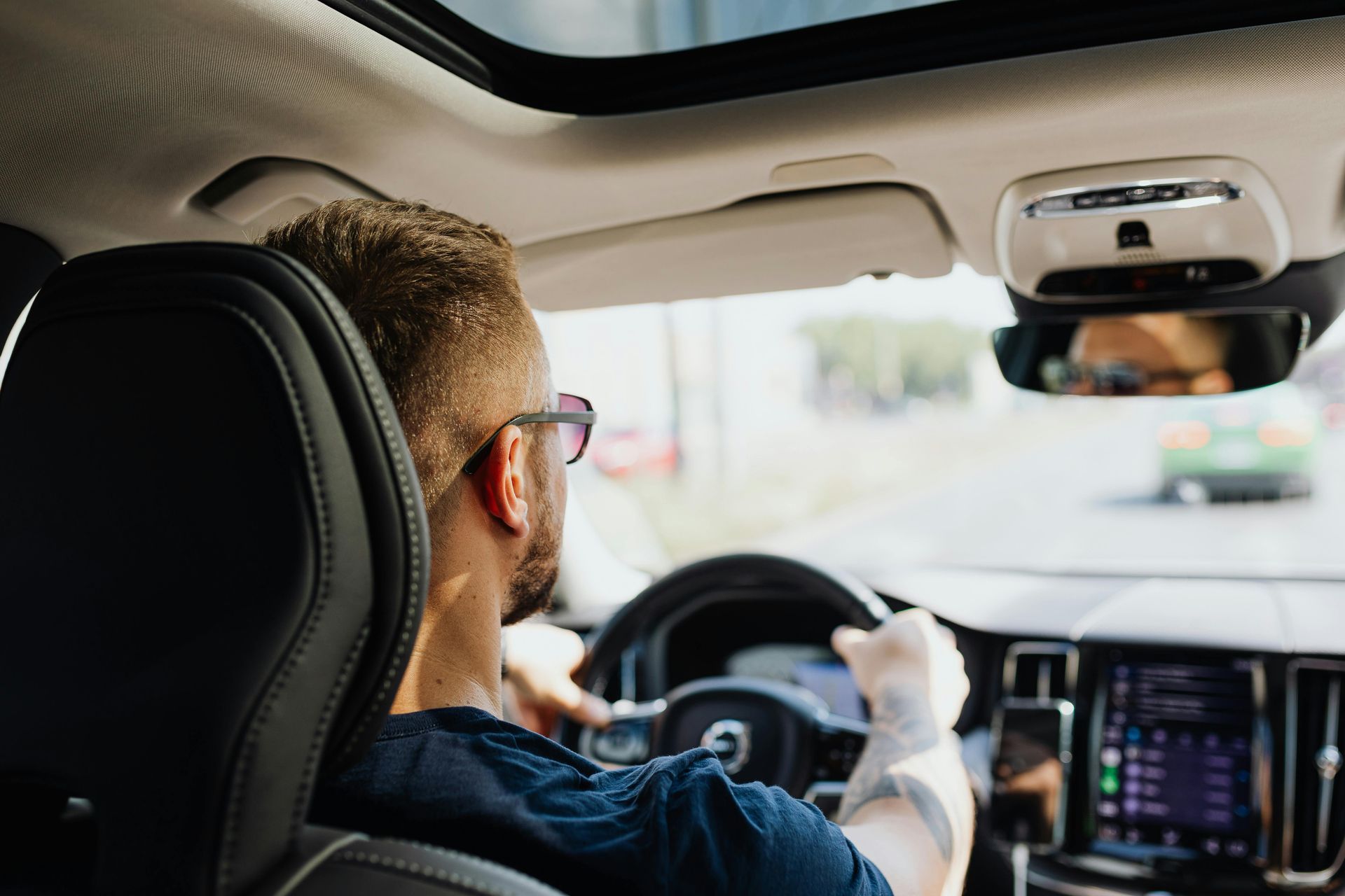 Driver holding a phone while driving a car, viewed from the back seat with dashboard display visible