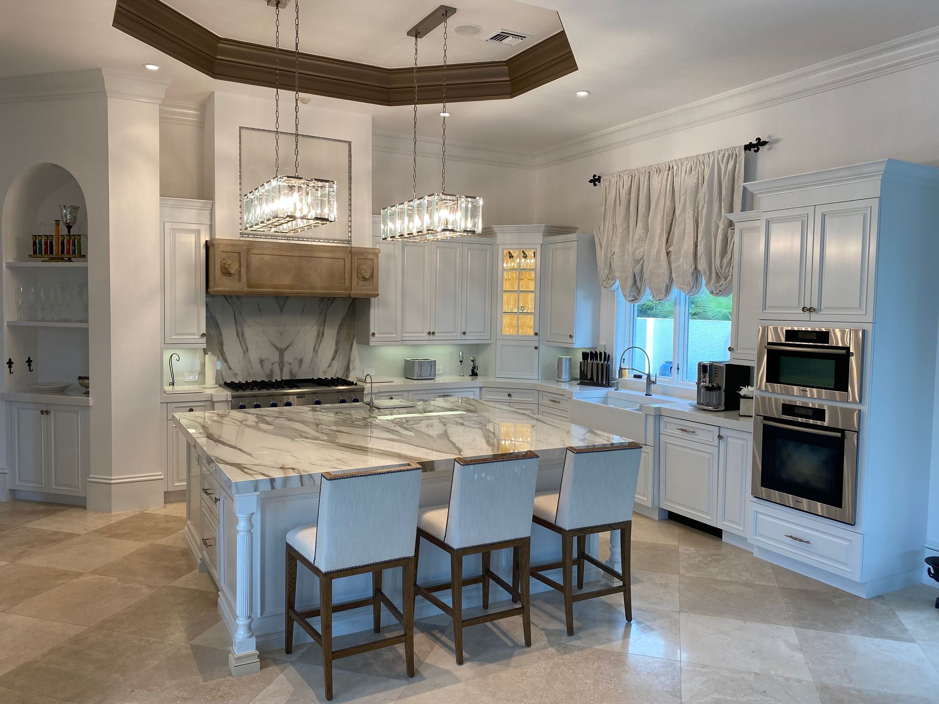 A kitchen with white cabinets , marble counter tops , stainless steel appliances and a large island.