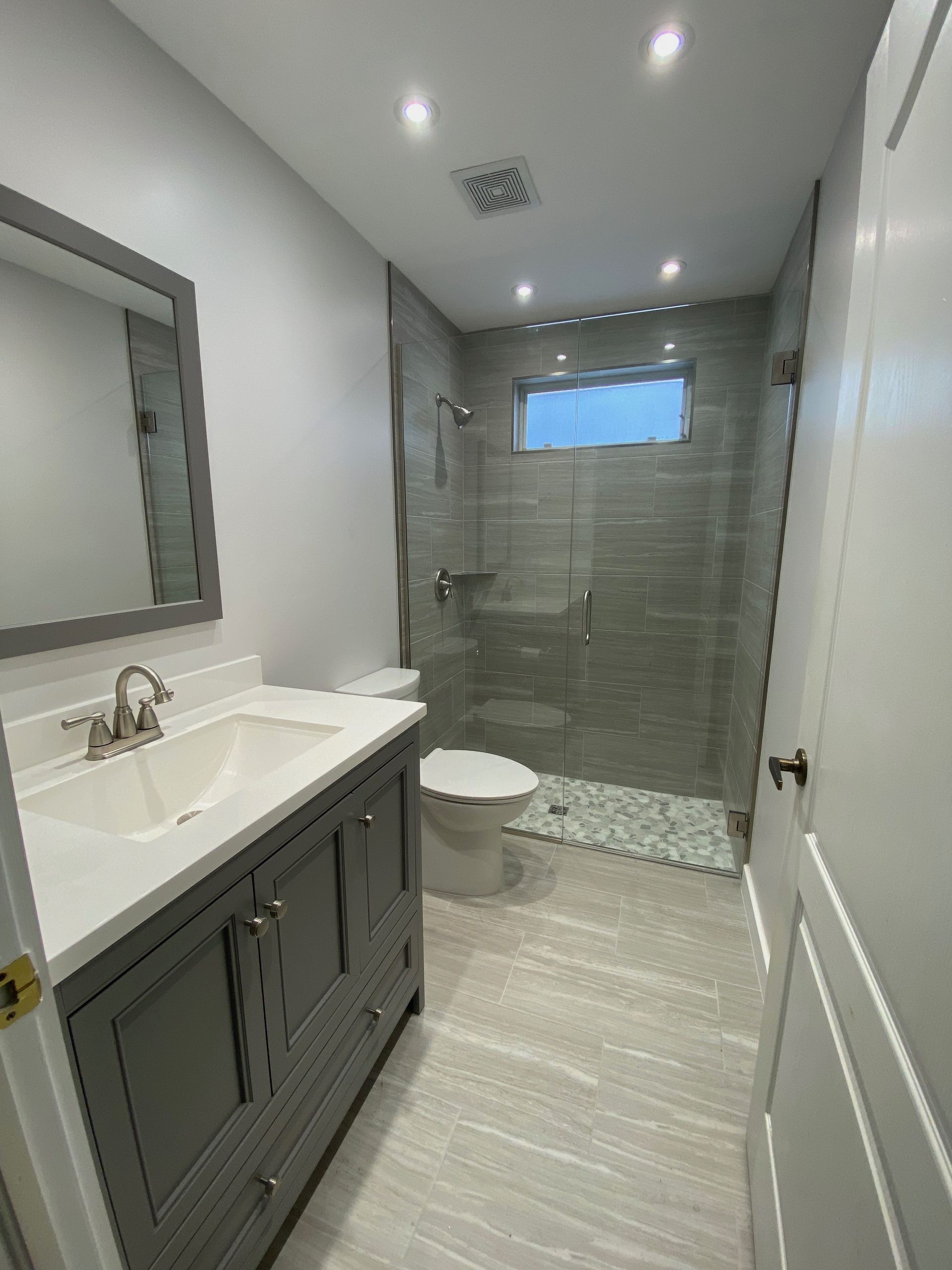 A bathroom with a sink , toilet , mirror and walk in shower.