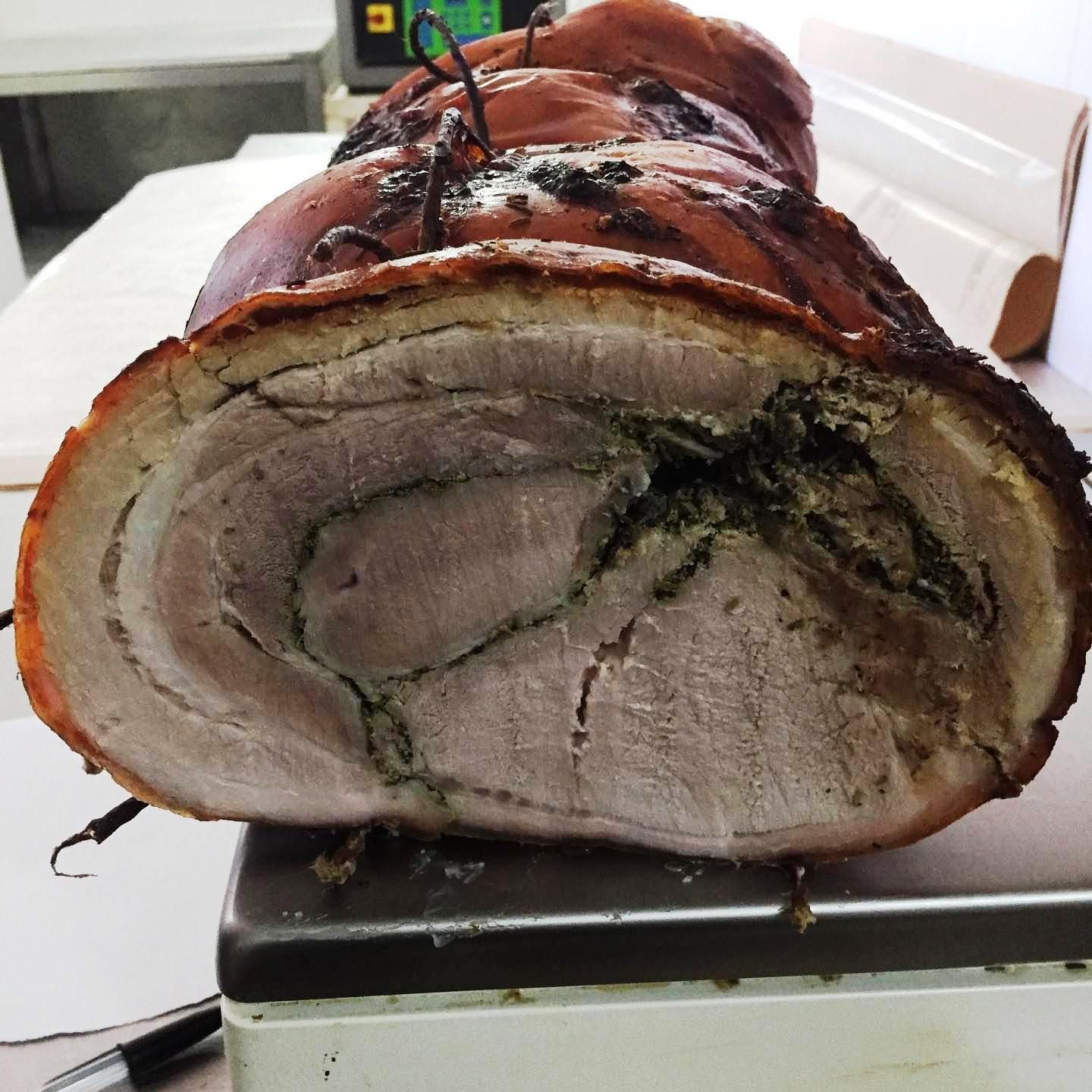 Una sezione trasversale di un rotolo di porchetta di maiale arrosto, ripieno di erbe aromatiche e con la crosta croccante e dorata, appoggiato su un bancone.