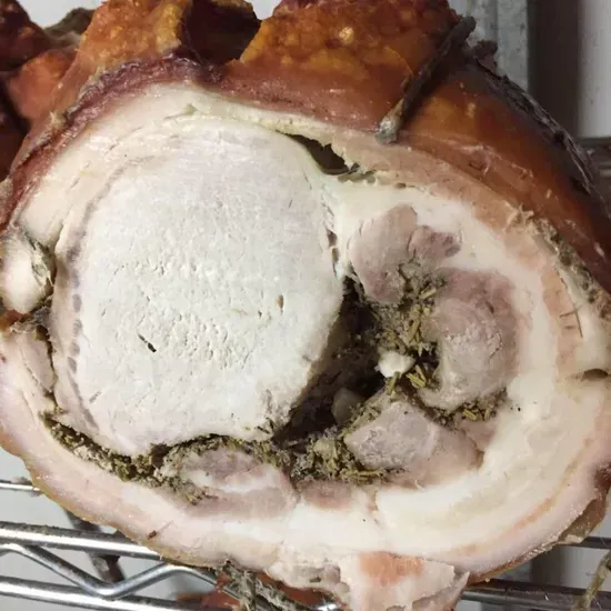 Un arrosto di maiale affettato e condito, con la cotenna croccante, arrotolato attorno a un cuore tenero su una griglia metallica.
