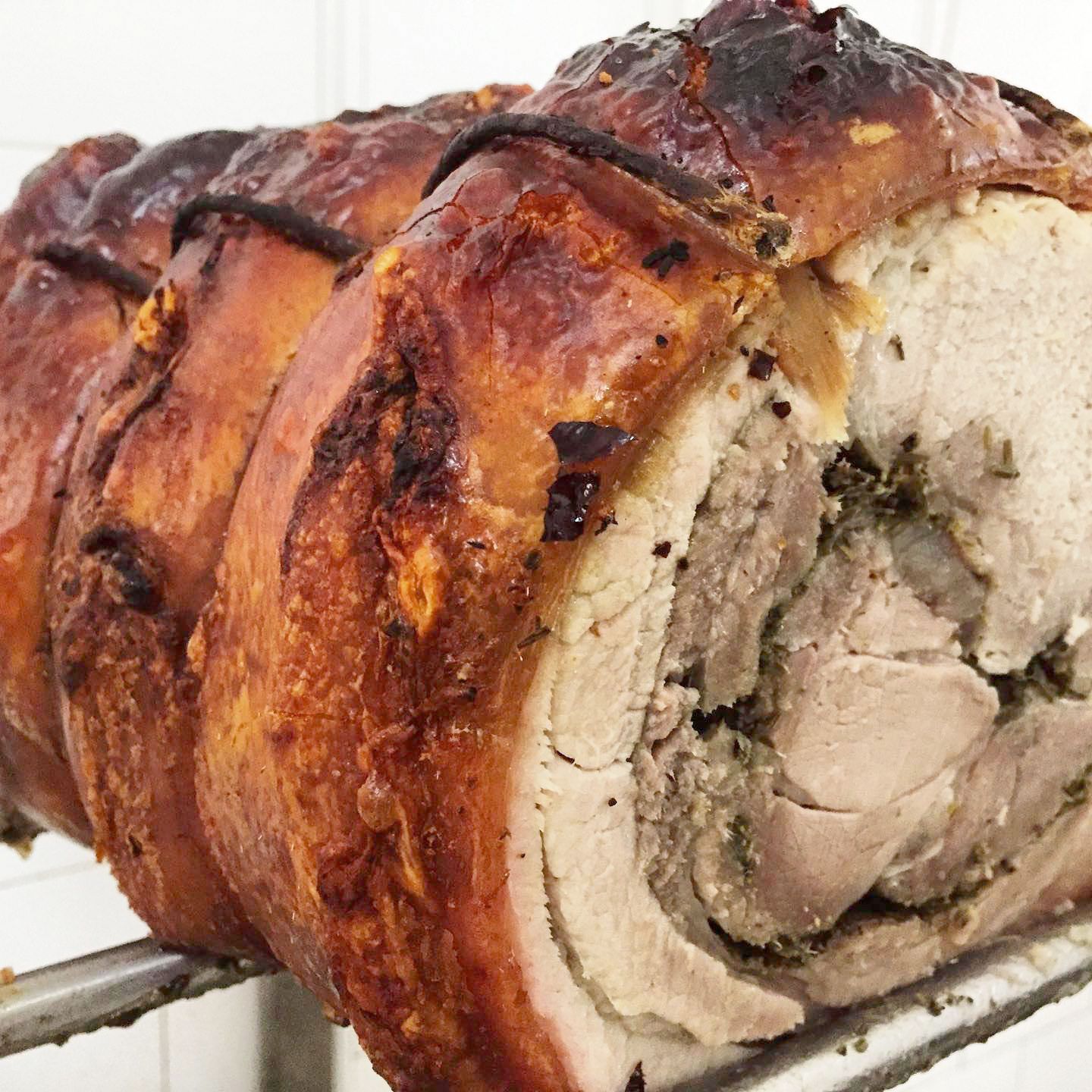 Una porchetta di maiale arrosto con la cotenna croccante e dorata, legata con dello spago e adagiata su una griglia metallica.