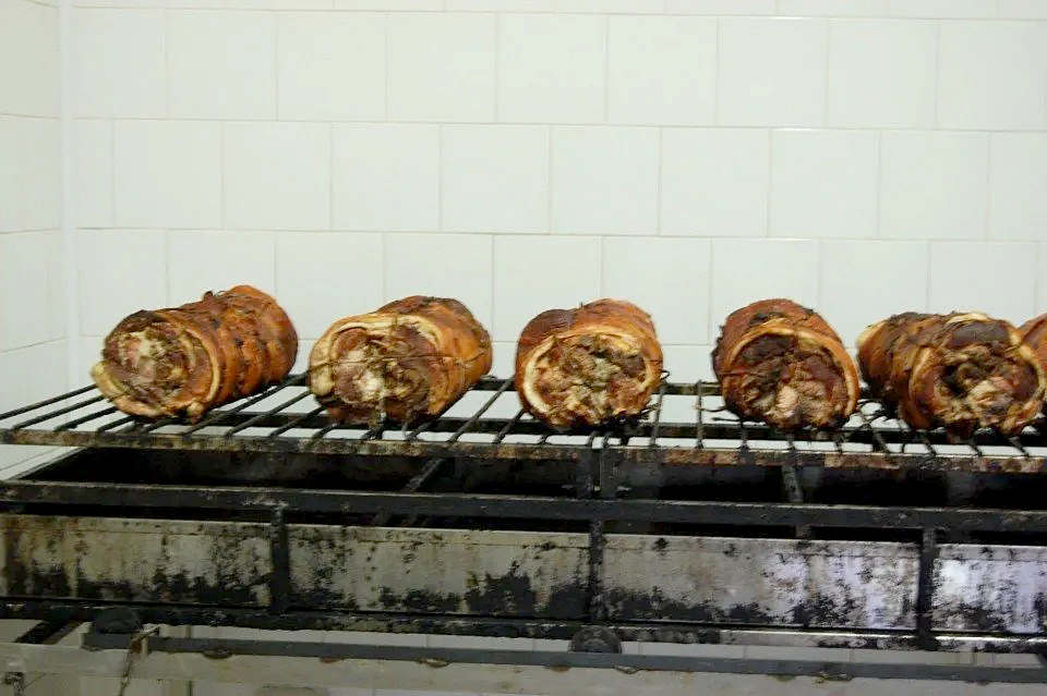 Cinque panini con porchetta arrosto allineati su una griglia metallica davanti a una parete piastrellata di bianco.