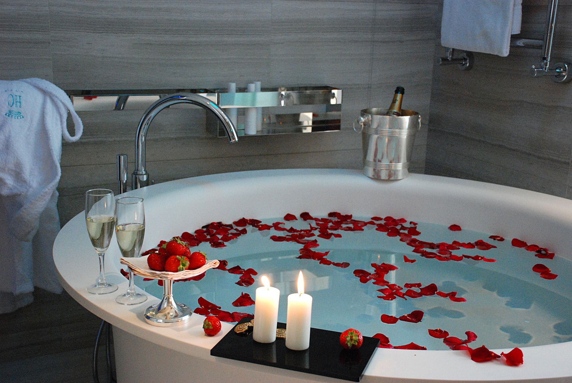 Круглая ванна, наполненная водой, разбросанные лепестки красных роз, два бокала шампанского, миска с клубникой и свечи.