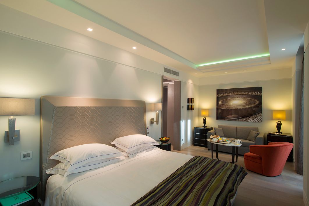 Современный минималистичный номер в отеле, оборудованный кроватью с узорчатым изголовьем, полосатой дорожкой и расположенной рядом зоной отдыха.