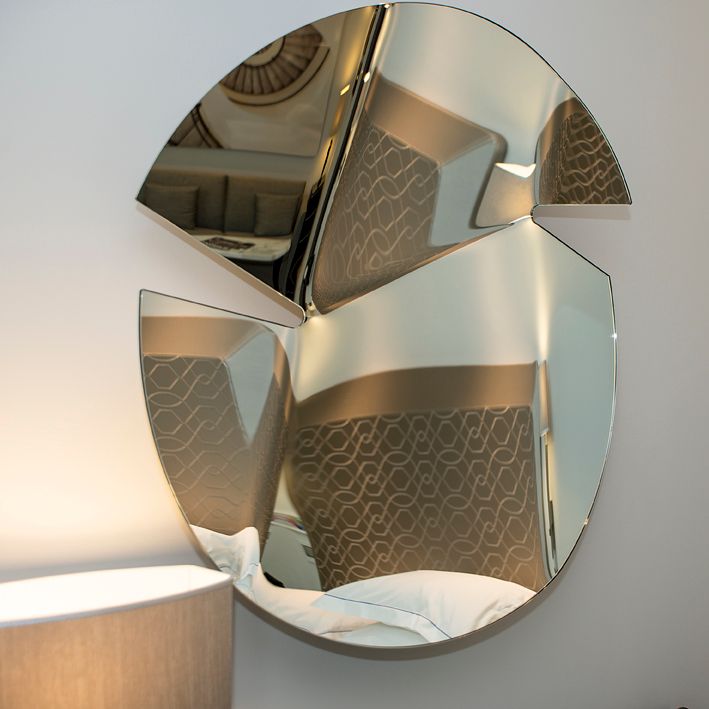 Современное настенное зеркало, состоящее из трех отдельных, расположенных под углом стеклянных сегментов, отражающих интерьер комнаты.