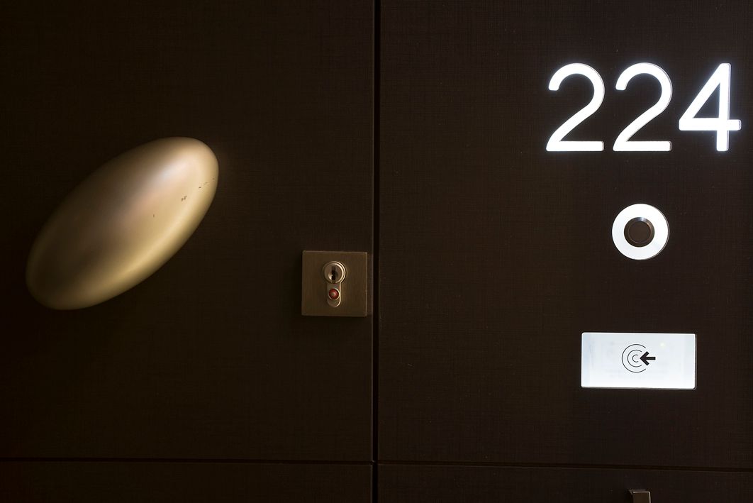 Темная дверь гостиничного номера с номером 224, золотой овальной ручкой, замочной скважиной, небольшим круглым светильником и электронным считывателем карт.