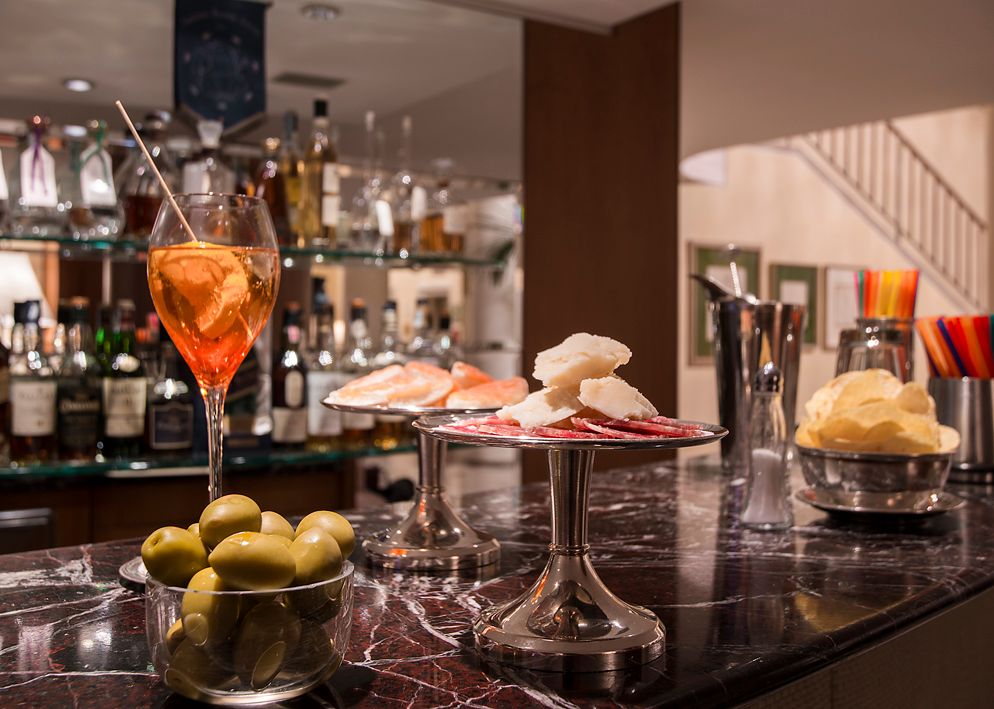 Коктейль, оливки, крекеры и чипсы, разложенные на мраморной барной стойке в приглушенно освещенном, высококлассном лаунже.