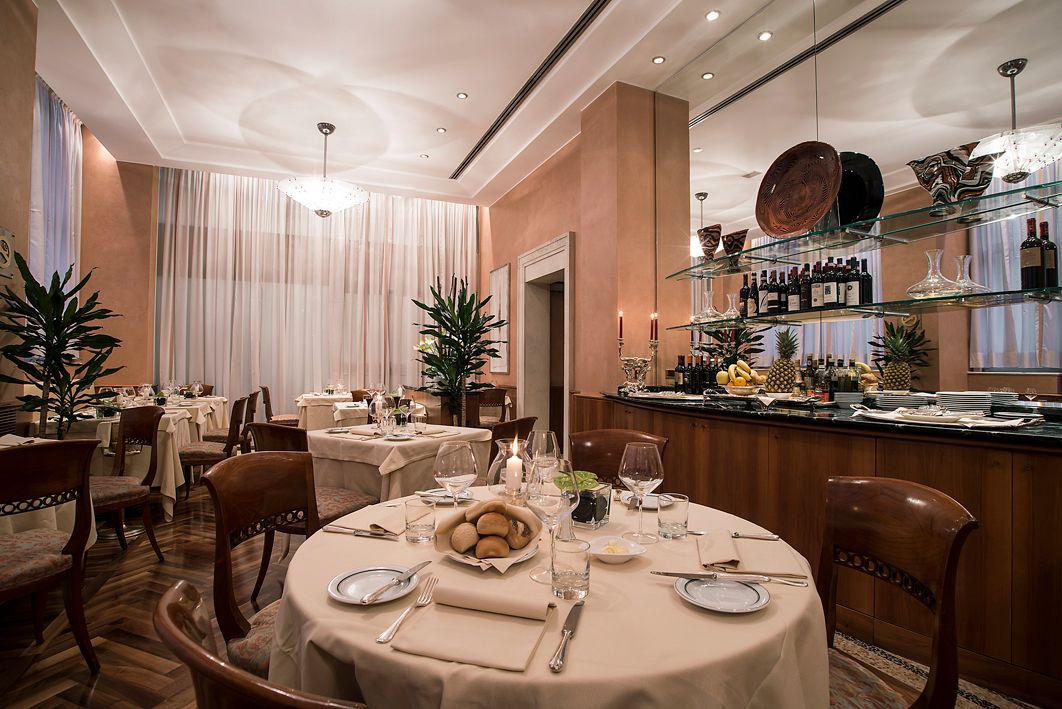 Уютный, элегантный обеденный зал ресторана с круглыми столами, покрытыми кремовыми скатертями, и деревянными стульями.