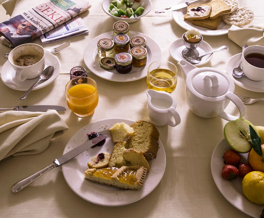 На завтрак был сервирован стол с разнообразной выпечкой, джемами, чайником, фруктами, чашкой кофе и газетой.