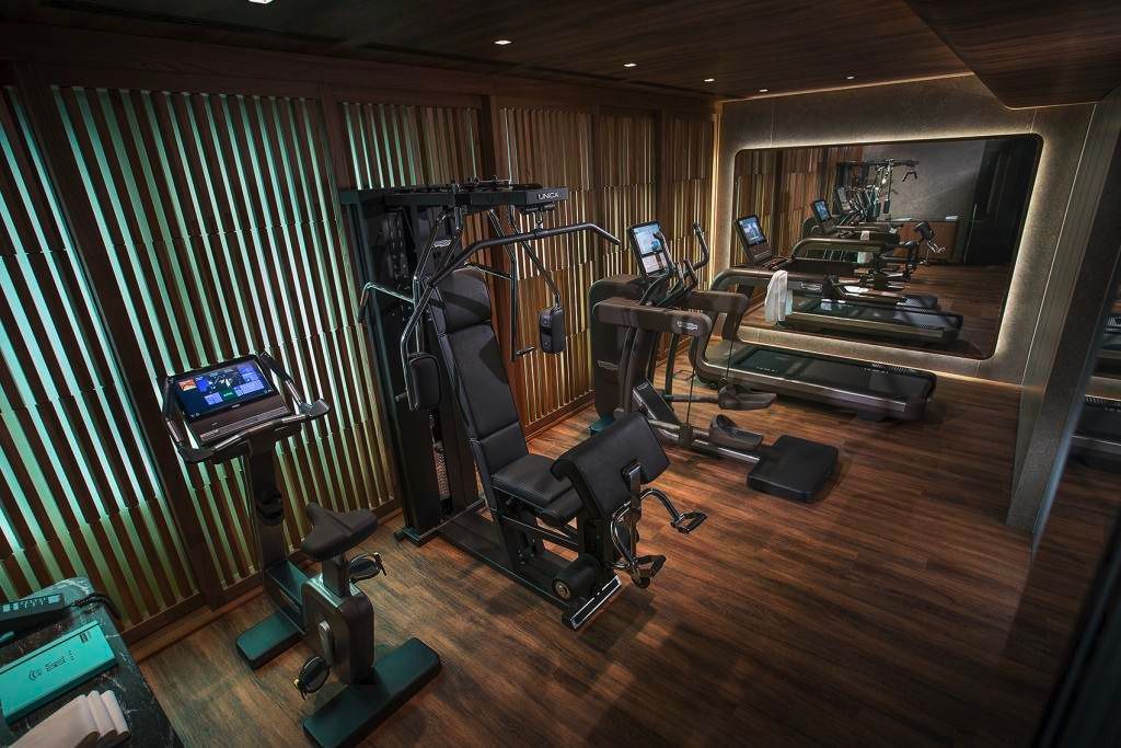 A modern, dark-toned home gym featuring a stationary bike, weight machine, elliptical, and a large wall mirror.