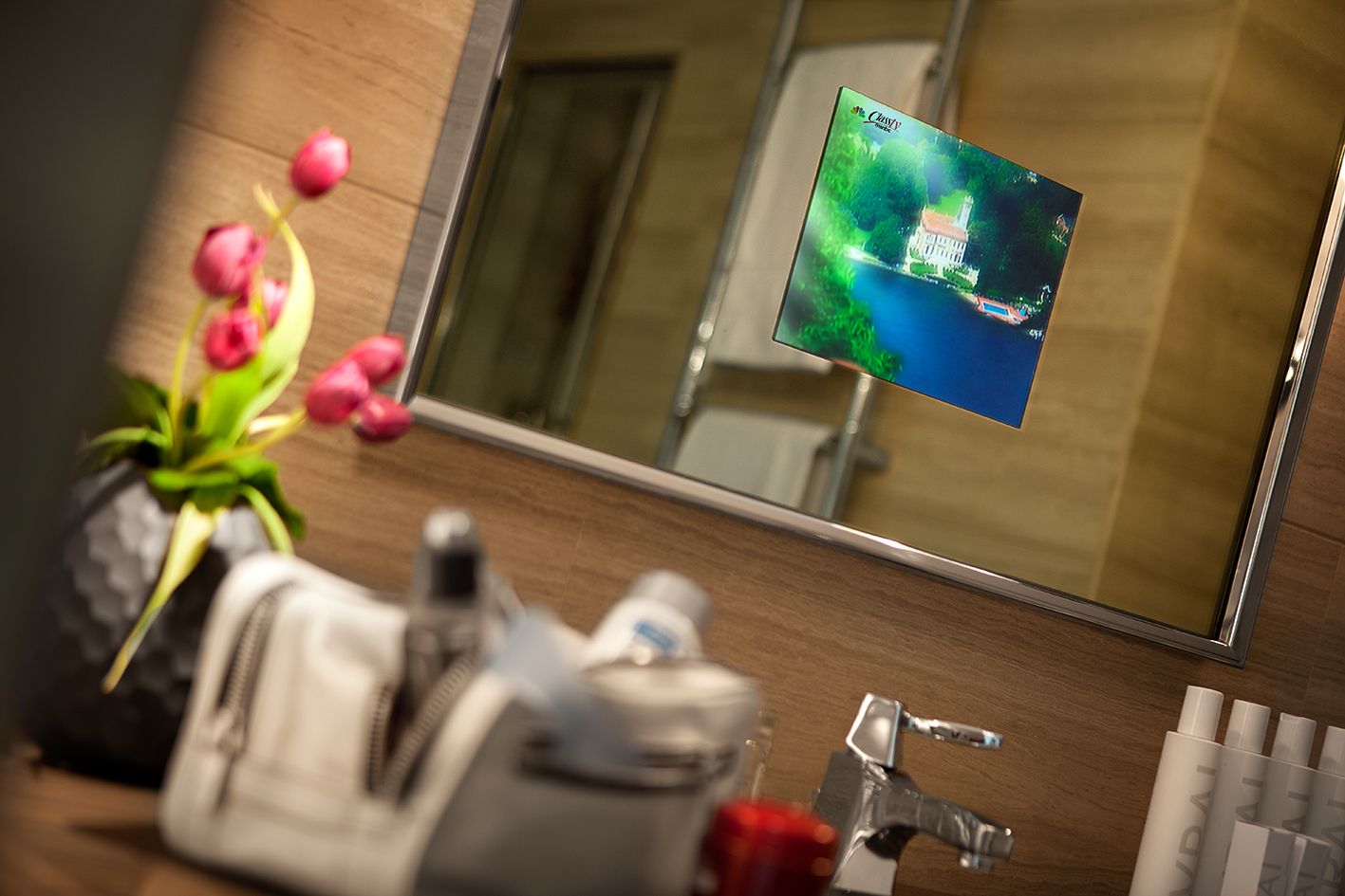 Ein eleganter Badezimmerspiegel zeigt eine lebendige Naturszene, darunter befinden sich eine Vase mit Tulpen und Toilettenartikel auf der Ablage.