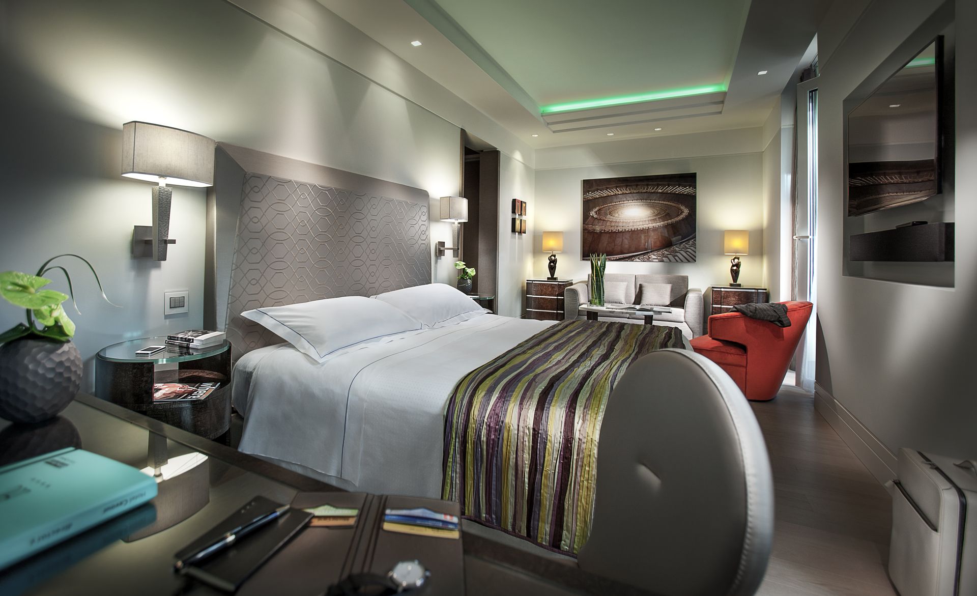 Современный, хорошо освещенный гостиничный номер с большой кроватью, фактурным изголовьем, полосатой дорожкой и ярким оранжевым креслом.