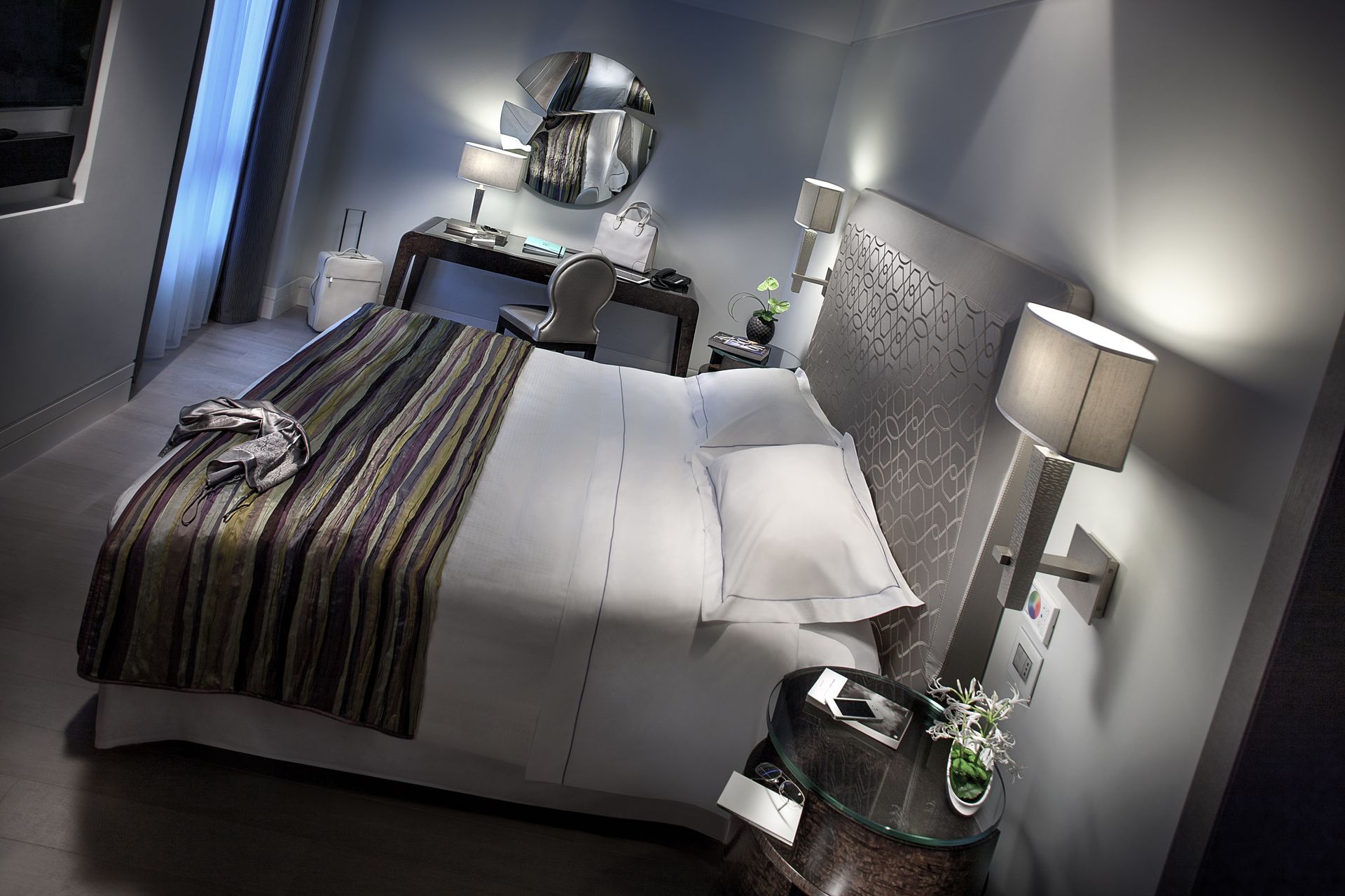 Современный гостиничный номер с двуспальной кроватью, полосатой ковровой дорожкой, туалетным столиком и современным освещением в нейтральной цветовой гамме.