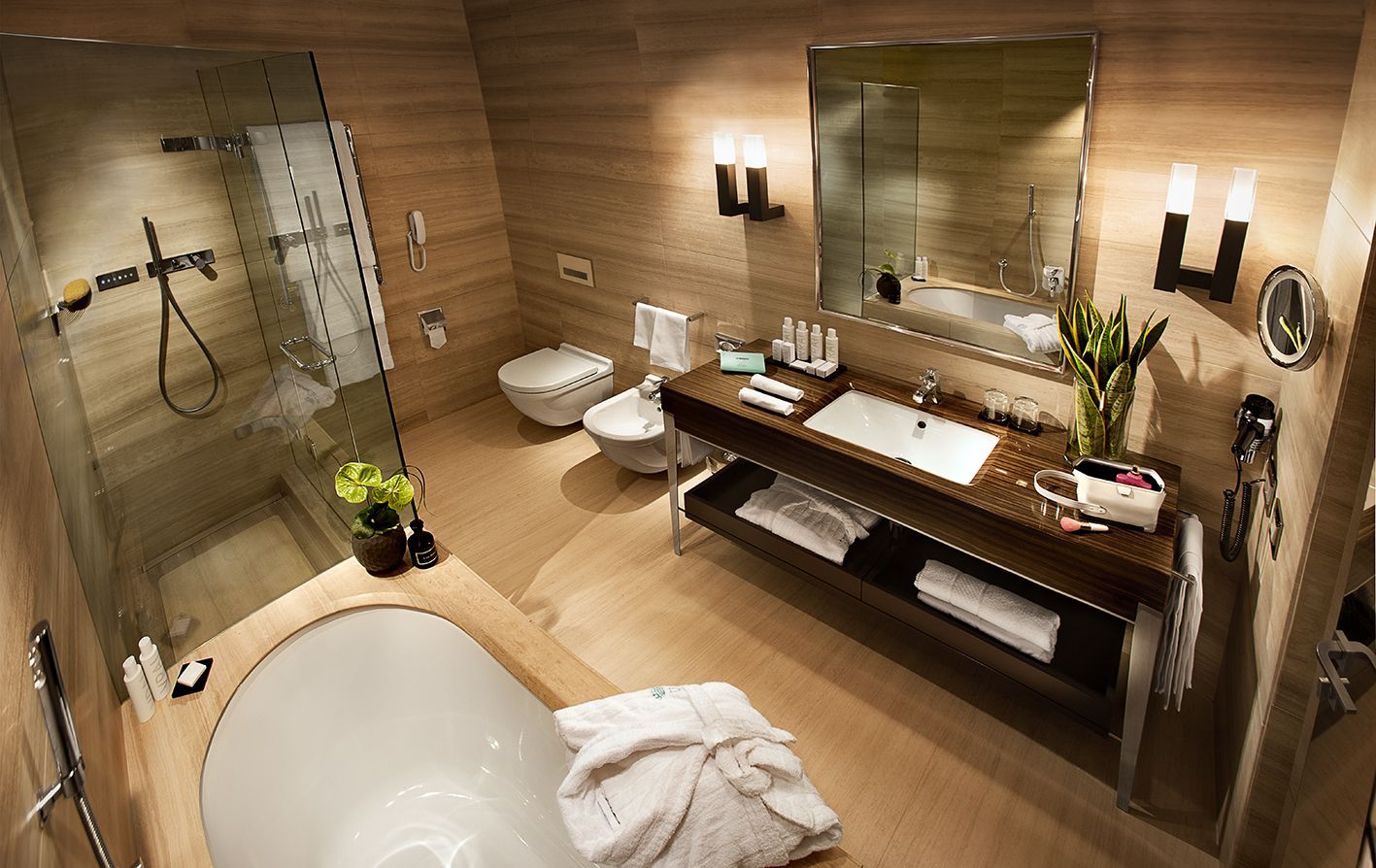 Современная ванная комната с ванной, стеклянной душевой кабиной, унитазом с двойным смывом, биде и одинарной раковиной с деревянной отделкой.