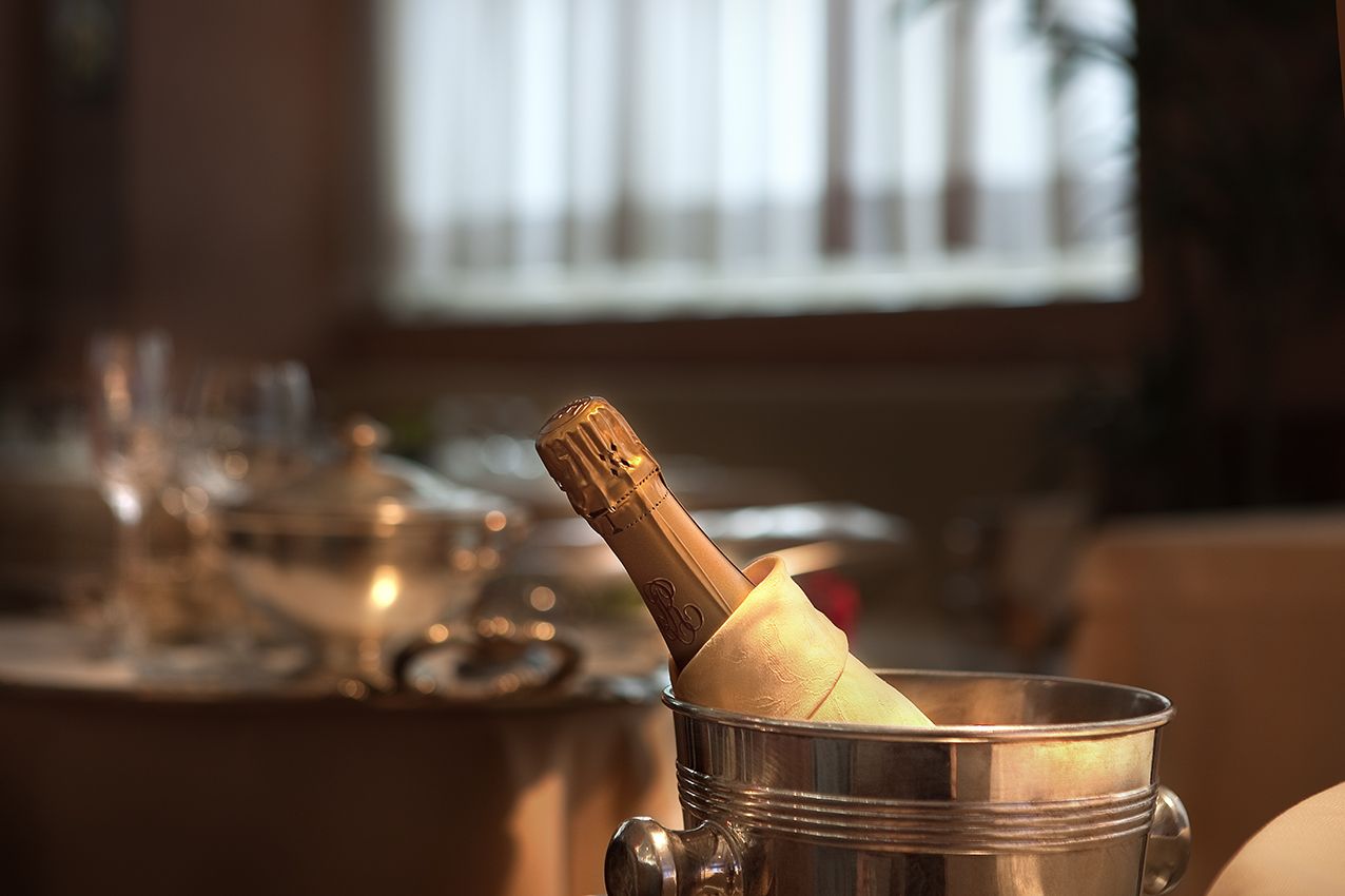 Бутылка шампанского в серебряном ведерке для льда на столе в тускло освещенном ресторане.