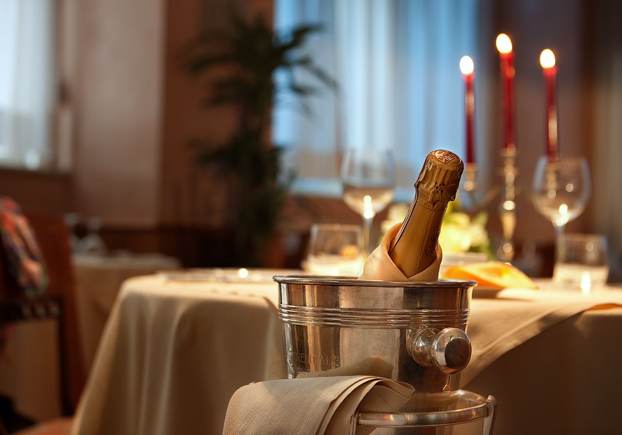 На столе, накрытом для романтического ужина с зажженными красными свечами, стоит бутылка шампанского в серебряном ведерке для льда.