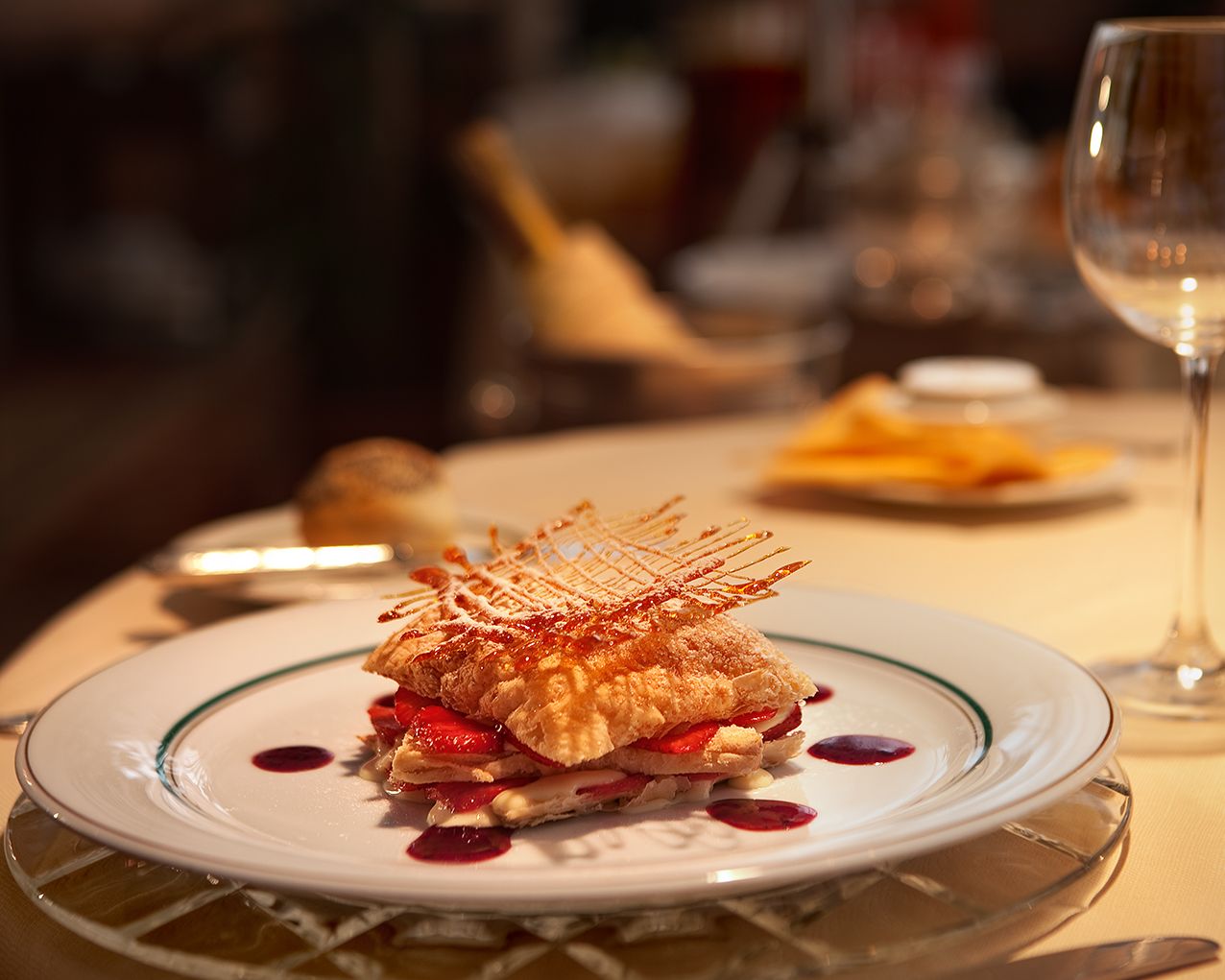 Элегантный мильфей с хрустящим тестом, красными ягодами и соусом на белой тарелке в ресторанной обстановке.