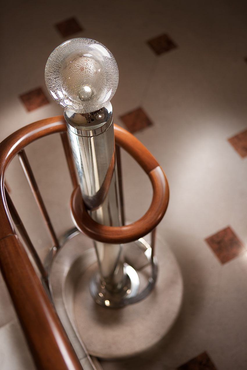 Деревянные перила в виде спирали изгибаются вокруг полированного металлического столба, увенчанного декоративным фактурным стеклянным шаром.