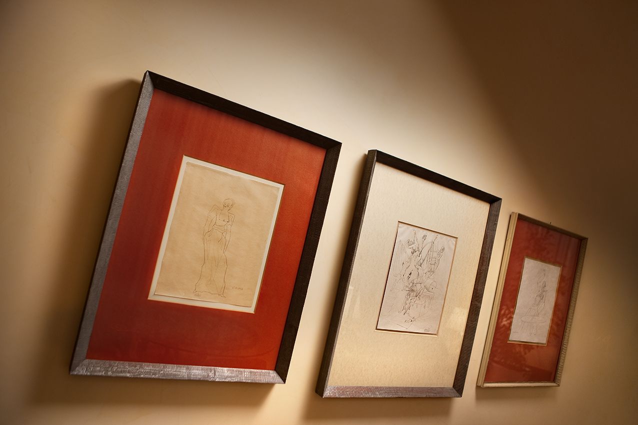 На светлой стене выставлены три эскиза в рамах с красно-белыми паспарту, снятые с нижнего ракурса.