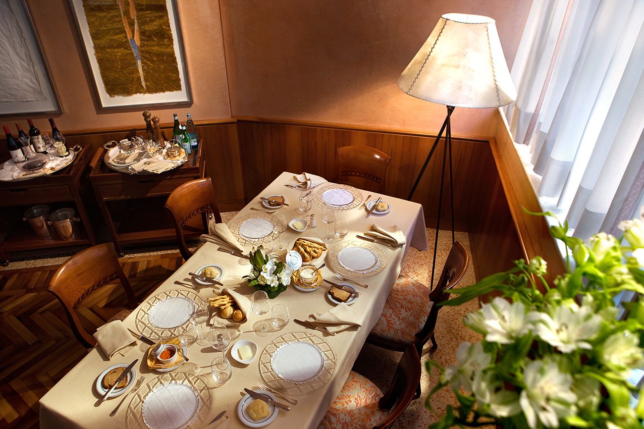 Элегантный обеденный стол, сервированный для трапезы в уютной комнате теплых тонов с деревянными панелями и высоким торшером.