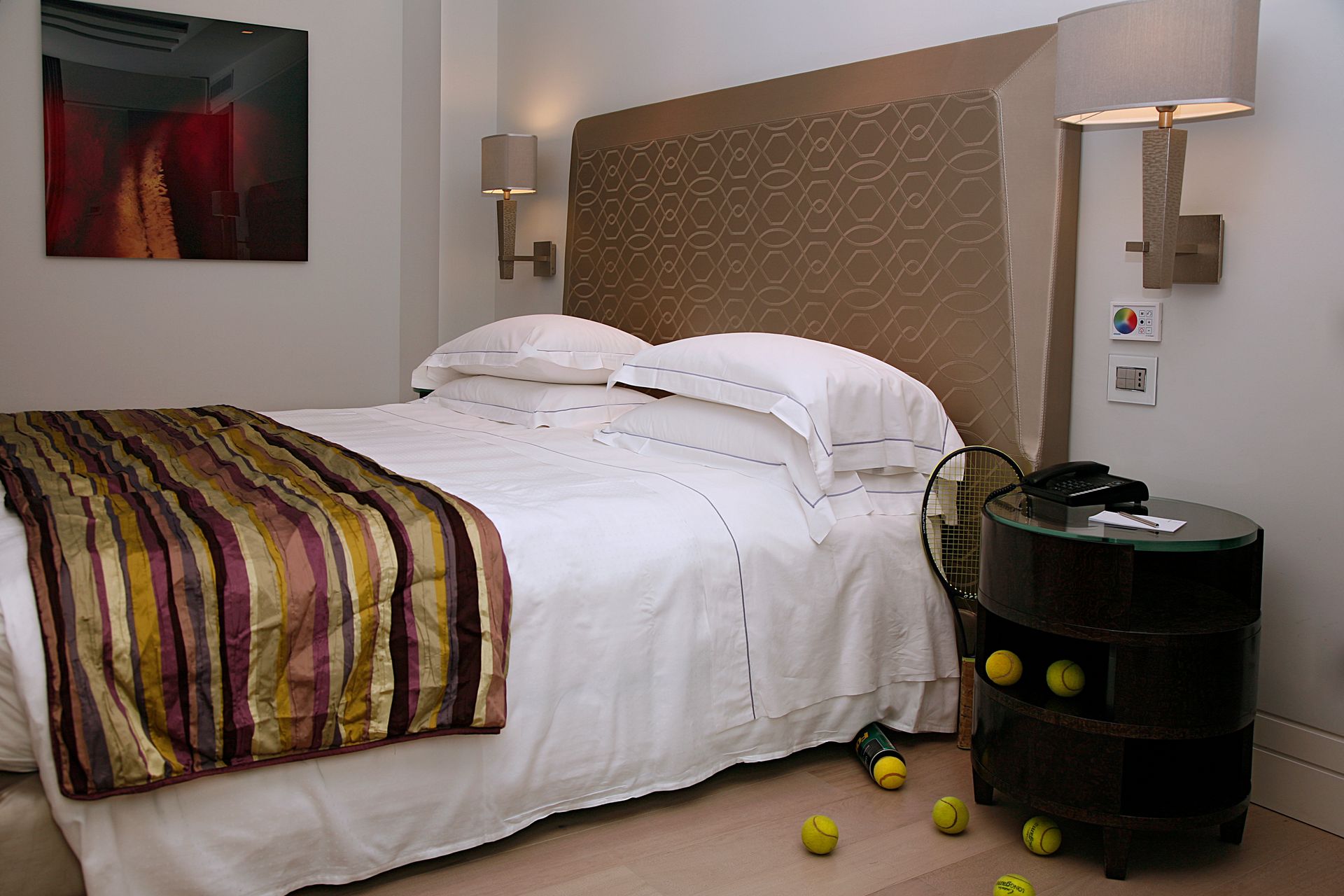 Спальня с кроватью, обитой бежевым изголовьем и покрытой полосатой дорожкой, рядом с черной многоярусной прикроватной тумбочкой, на которой разбросаны лимоны.