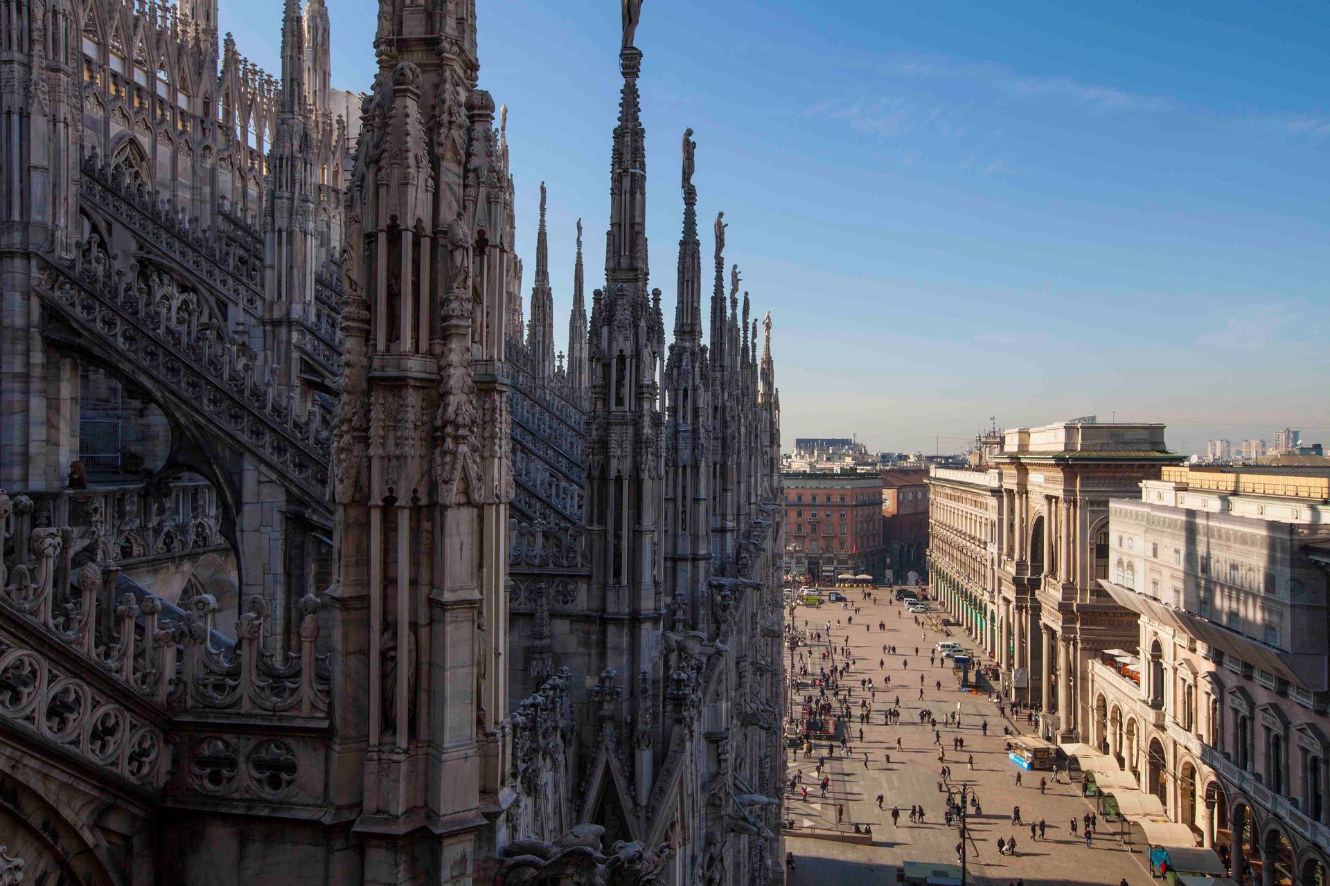View from above looking down at the ornate spires of the Milan Cathedral and the bustling square below.
