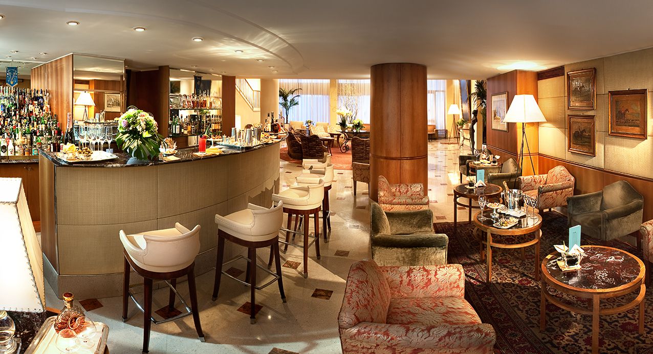Панорамный вид на элегантный лобби-бар отеля с изогнутыми сиденьями, креслами с узорами и теплым рассеянным освещением.
