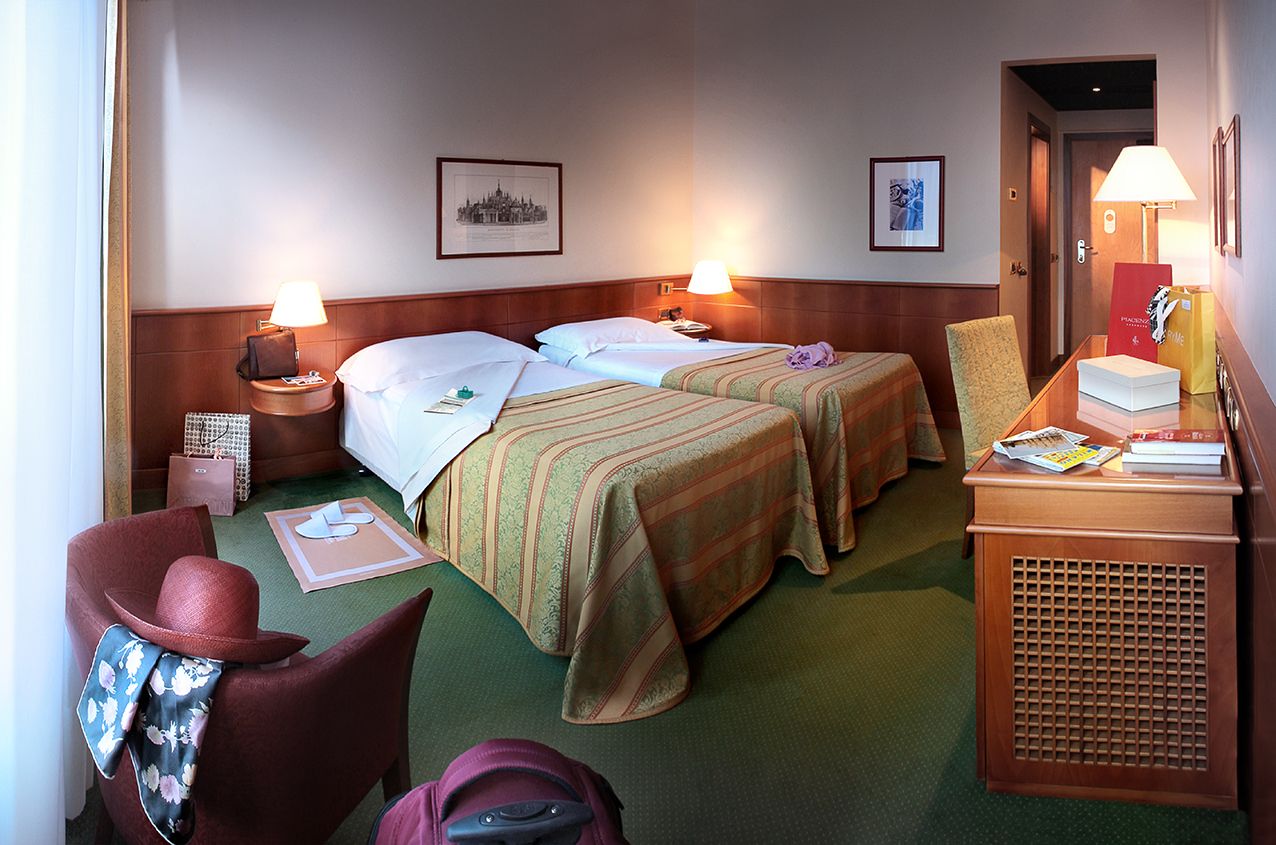 В гостиничном номере были две односпальные кровати, зеленый ковер, деревянный стол и кресло, а также шляпа и шарф.