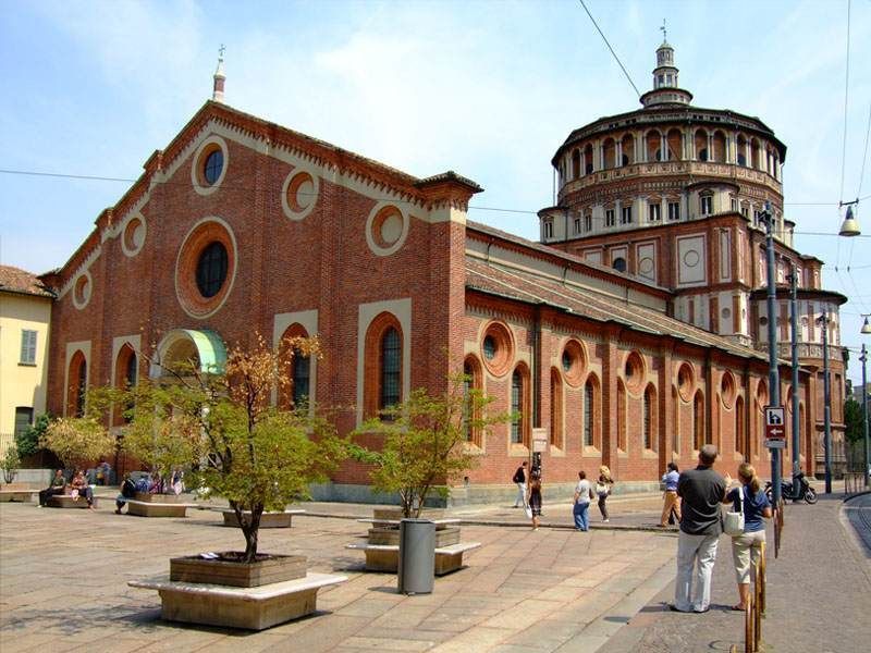 The red brick Santa Maria delle Grazie church in Milan, featuring its distinct Renaissance dome and a paved courtyard.