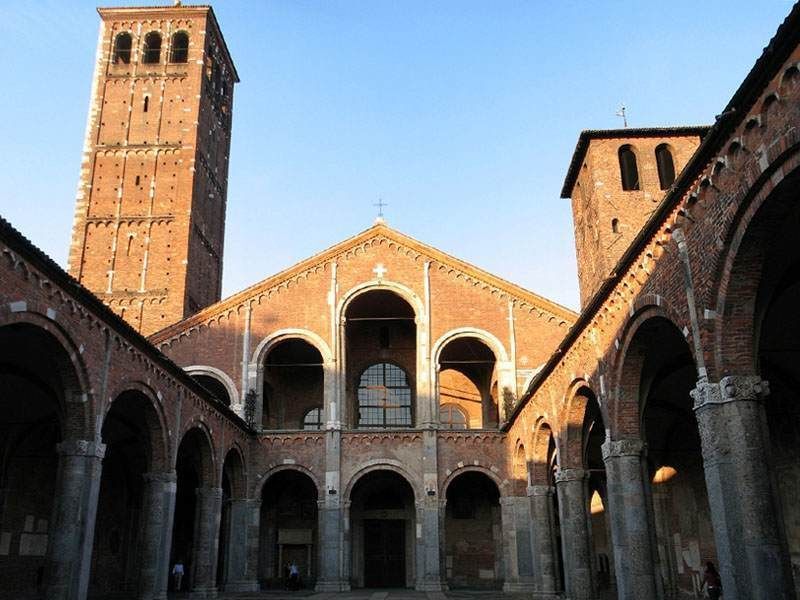 The Basilica of Sant'Ambrogio in Milan featuring a brick courtyard, arched walkways, and two bell towers.