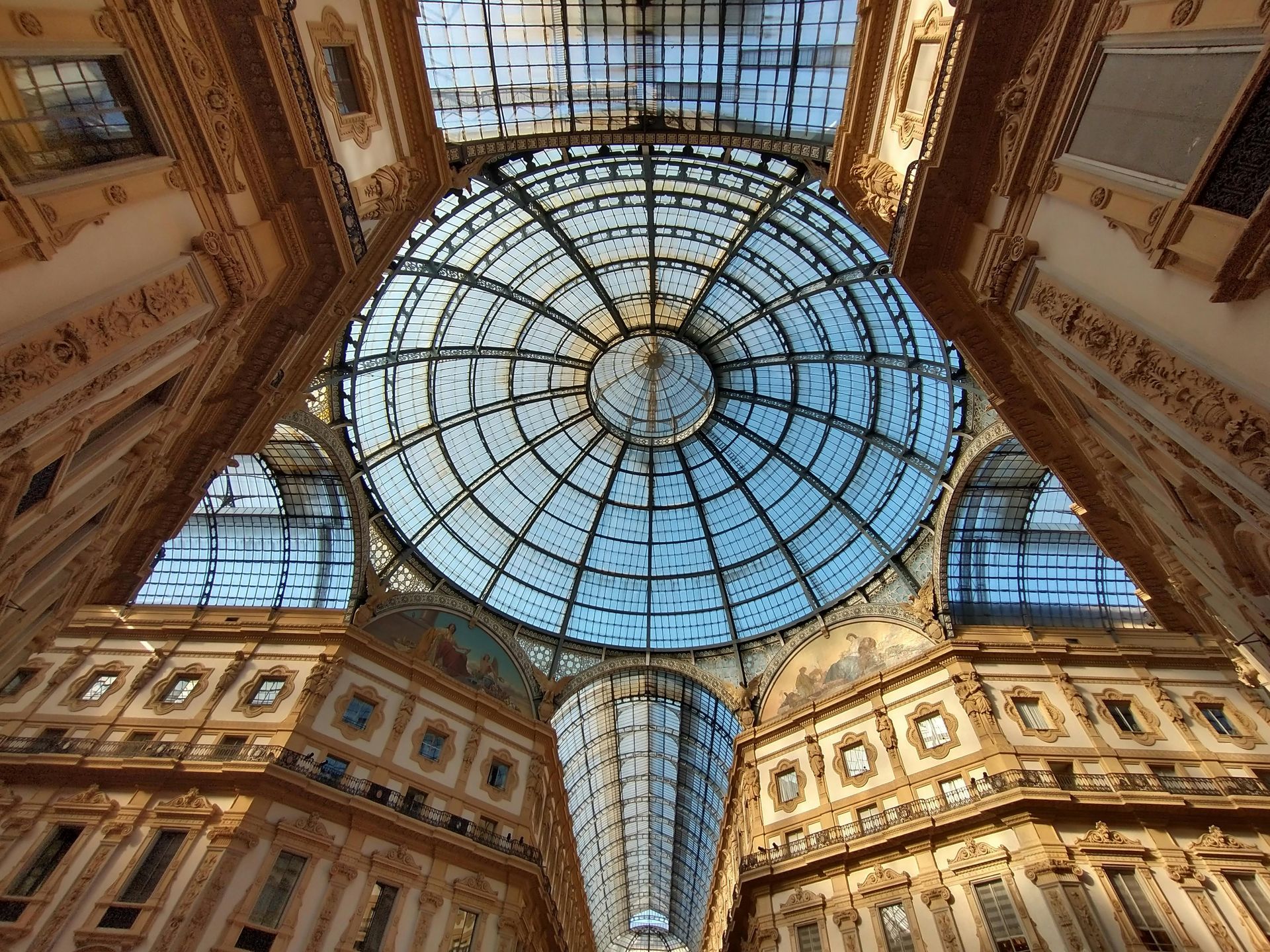 Looking up at the ornate glass dome and arched ceilings of the Galleria Vittorio Emanuele II in Milan.