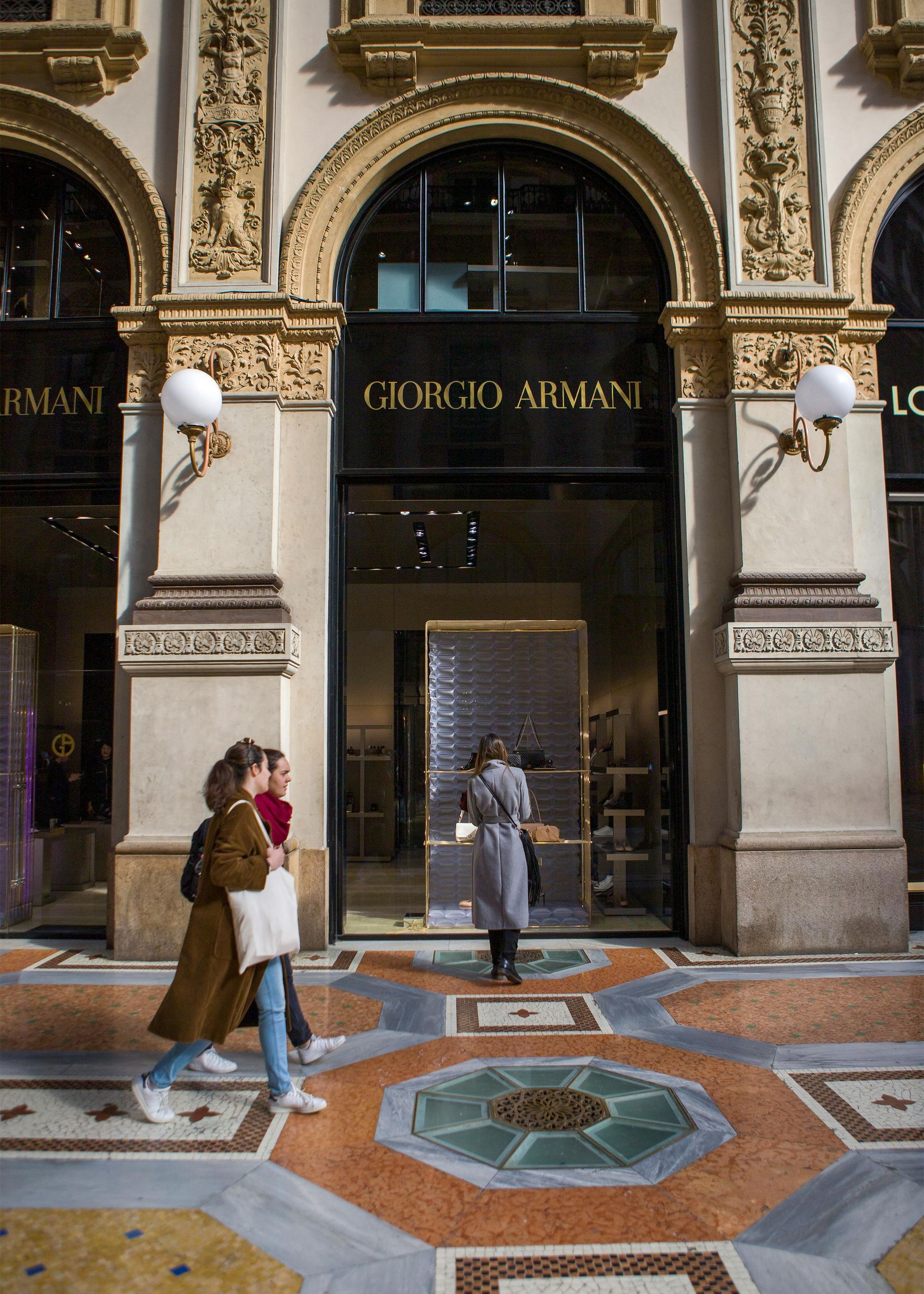 两人走过乔治·阿玛尼 (Giorgio Armani) 商店入口,该入口采用古典建筑风格,并饰以华丽的黄金装饰。