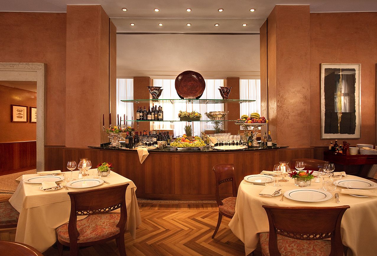 Элегантный интерьер ресторана с сервированными столиками, стенами теплых тонов и центральной буфетной станцией под мягким освещением.