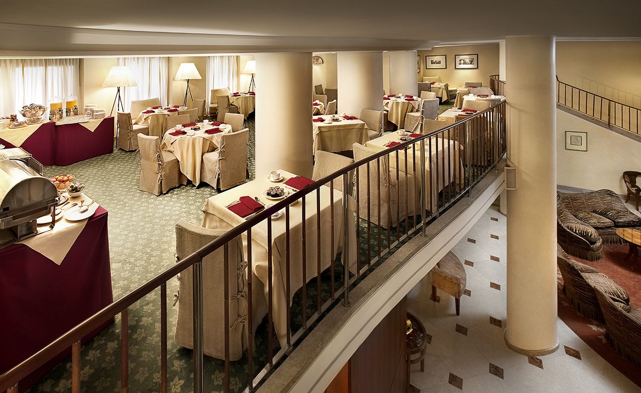 Многоуровневый ресторан со столиками, накрытыми кремовыми скатертями и бордовыми салфетками, вид с огороженного балкона.