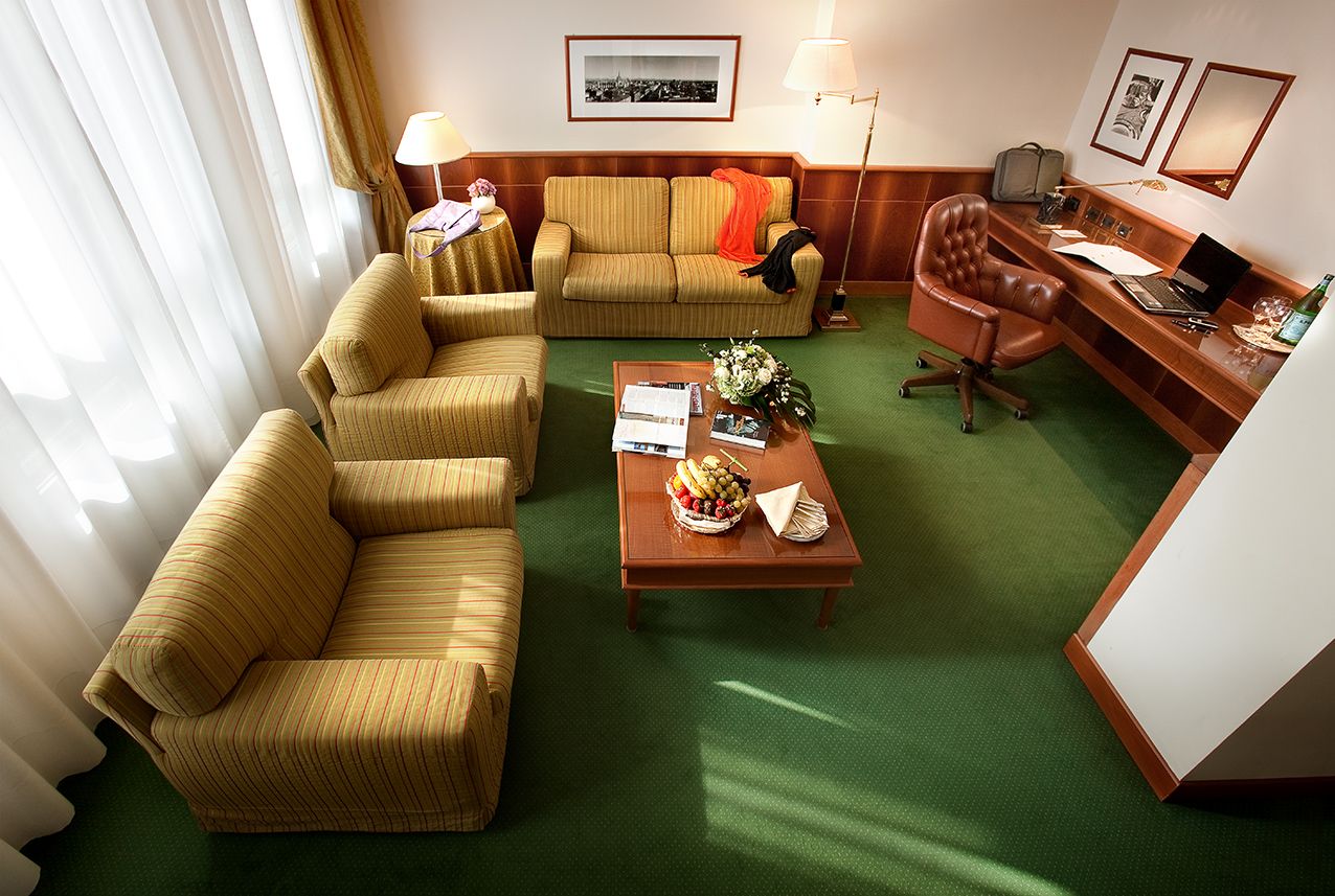 Вид сверху на гостиничный номер с желтой тканевой обивкой, деревянным журнальным столиком, письменным столом и зеленым ковровым покрытием.