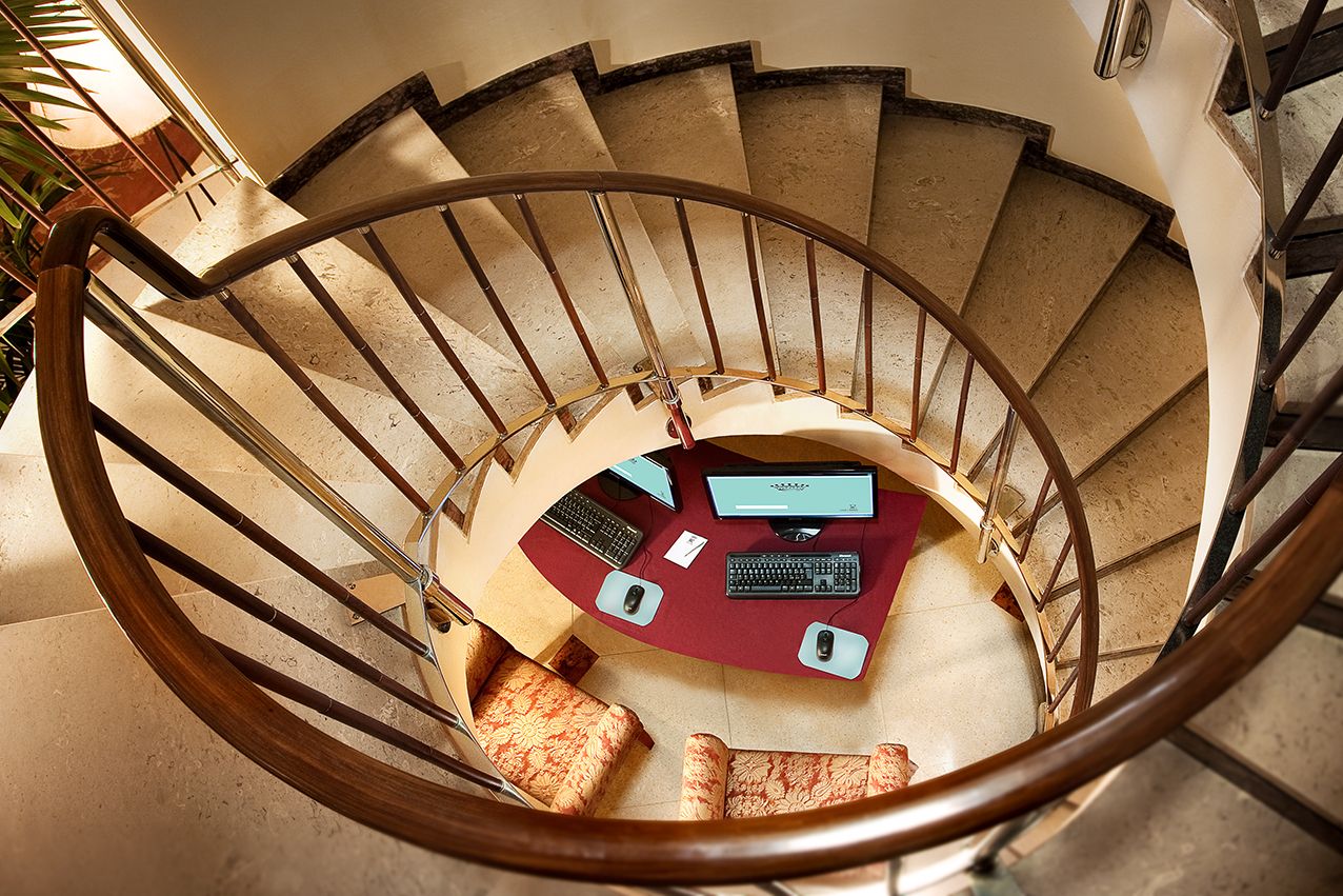 Вид сверху вниз по винтовой лестнице на небольшой стол, под которым расположен компьютер.