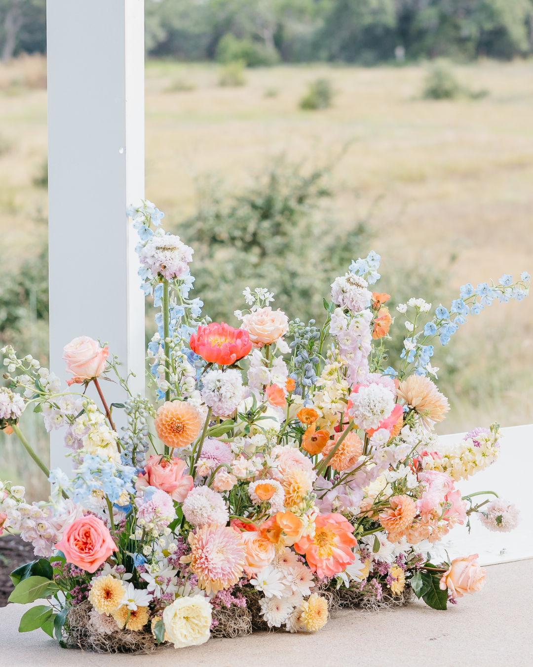 Outdoor wedding ceremony setting with rows of wooden chairs, a stone aisle, and a floral-decorated arch against a field.