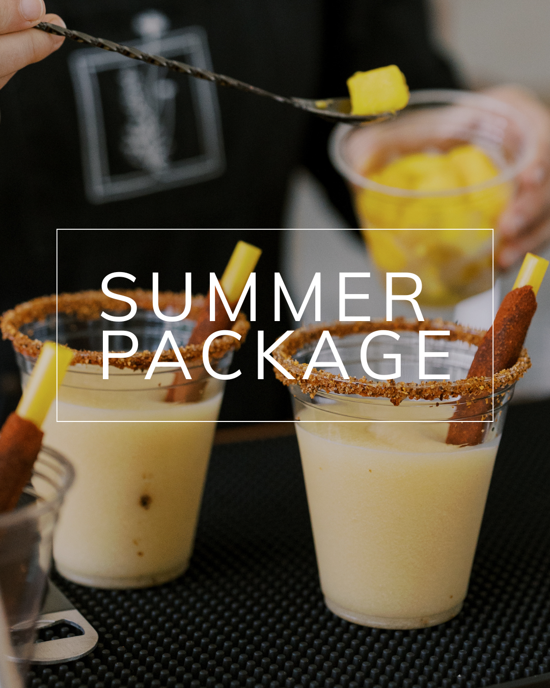 Two cups of light-colored slushy drinks with chili-rimmed edges and tamarind sticks, beside a bowl of fresh mango cubes.