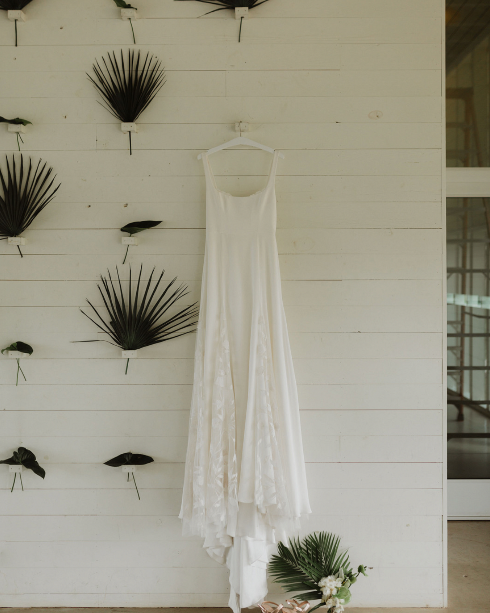 A white dress is hanging on a hanger on a white wall.