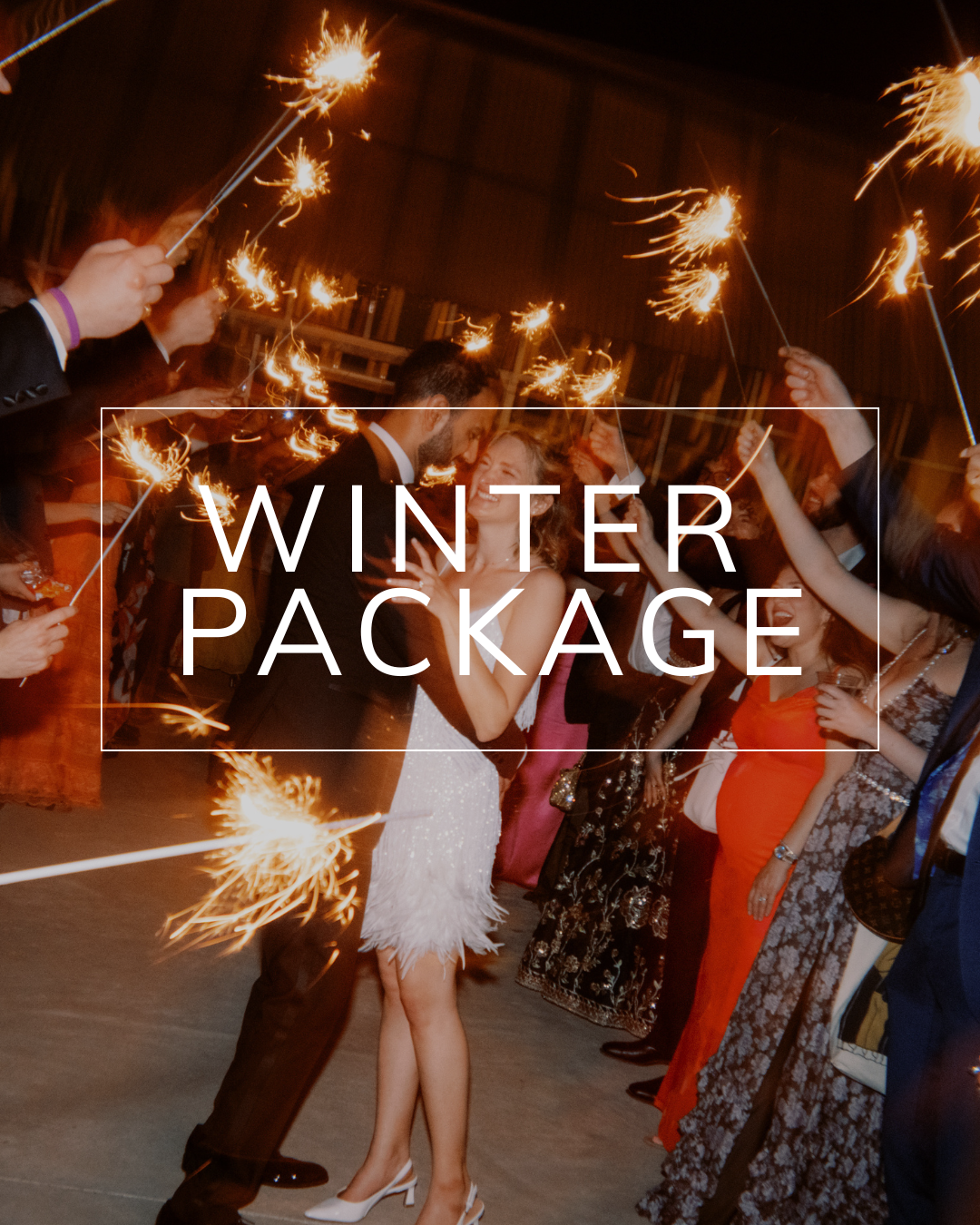 A couple dancing at night while surrounded by guests holding sparklers, with