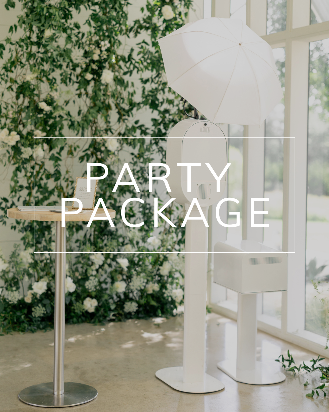 A white photo booth set up for an event, placed in front of a floral wall and next to a small table.